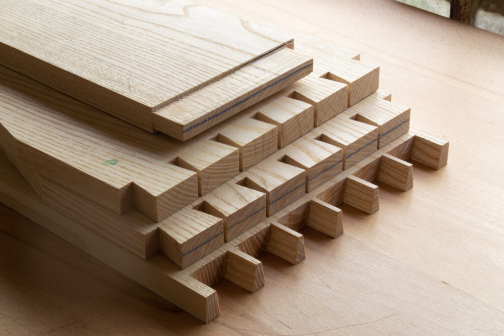 Pièces de bois en frêne avec assemblages en queue d’aronde prêts à être montés, posés sur un établi.